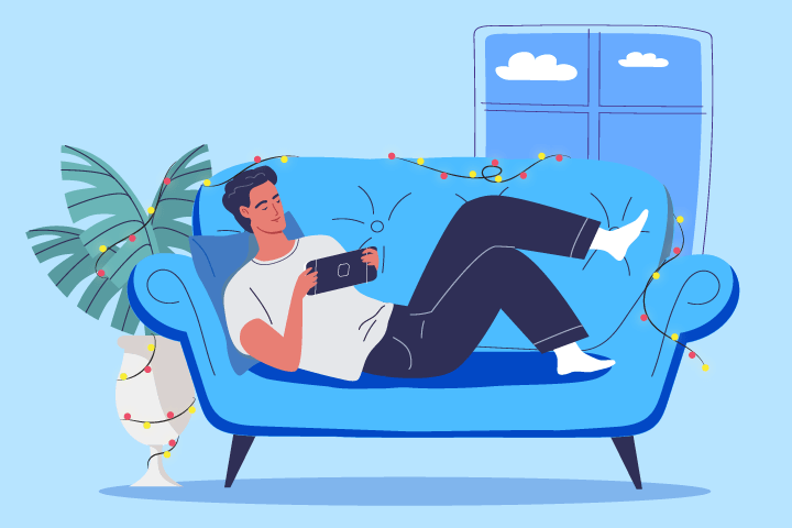 person relaxing on a couch playing video games surrounded by holiday lights
